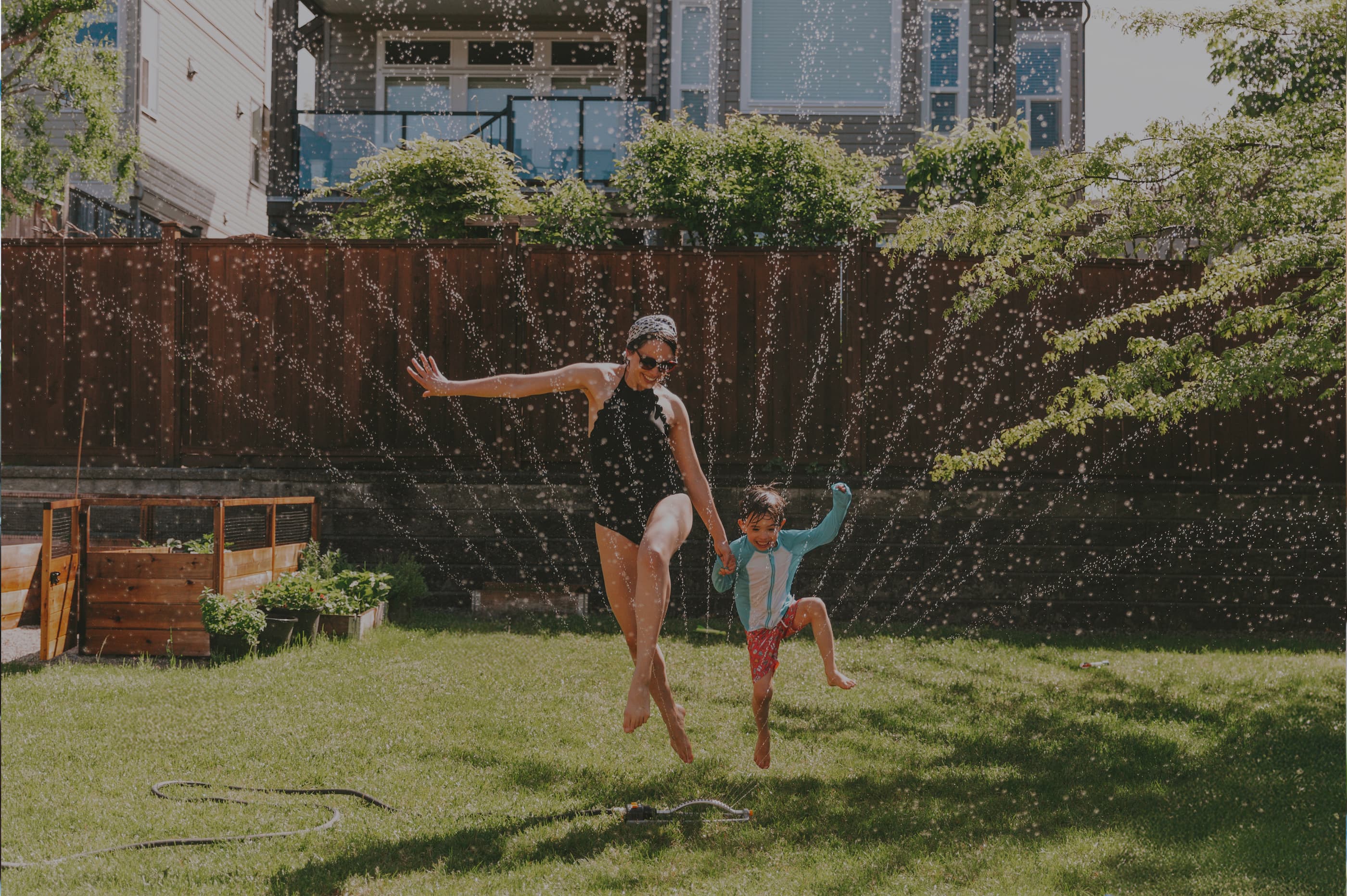 Mother and child playing on a lawn with a sprinkler